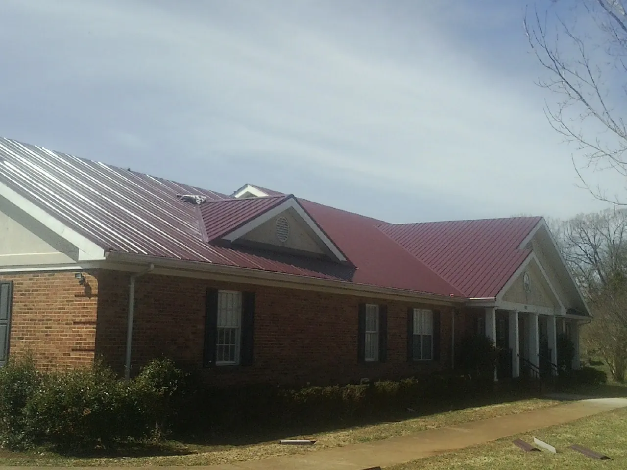 Red metal roof with gabled entries on a long brick building, from a Hail Damage Roof Repair job in Hiawassee