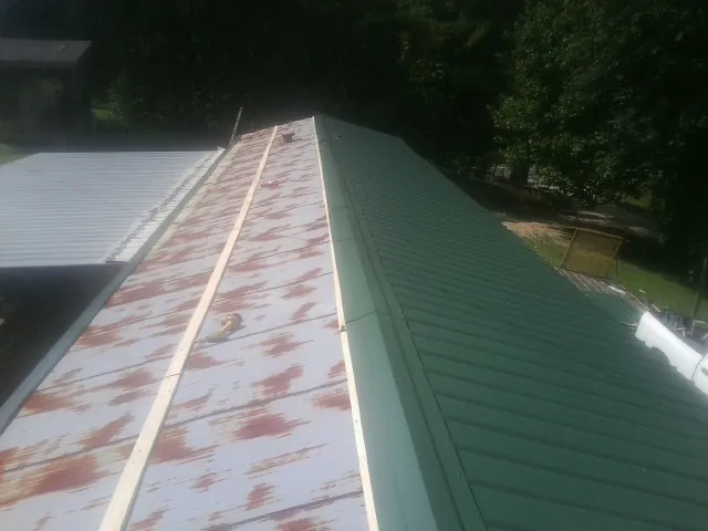 Old rusted panels beside newly installed green metal roofing — Wind Damage Roof Repair by Roofing Brothers in Hiawassee