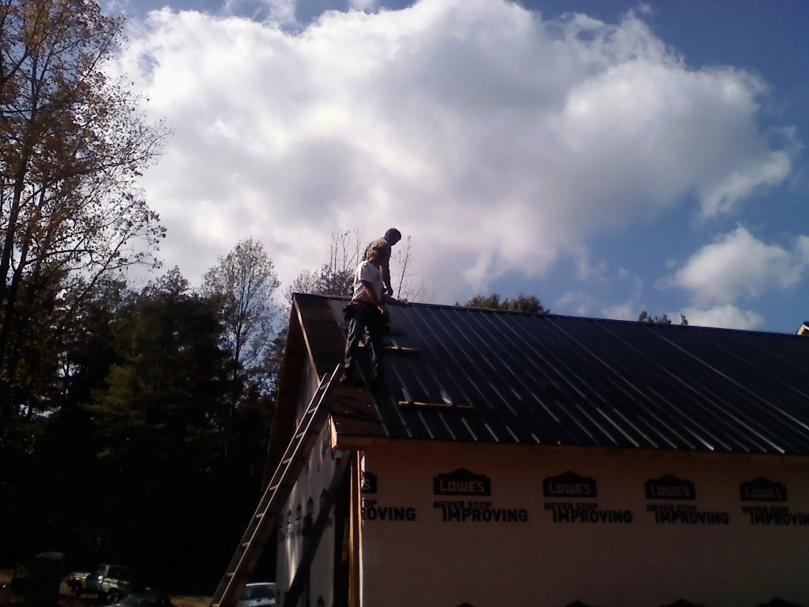 Roofer fastening dark metal panels high against a cloudy sky, from a Roof Inspection job in Hiawassee