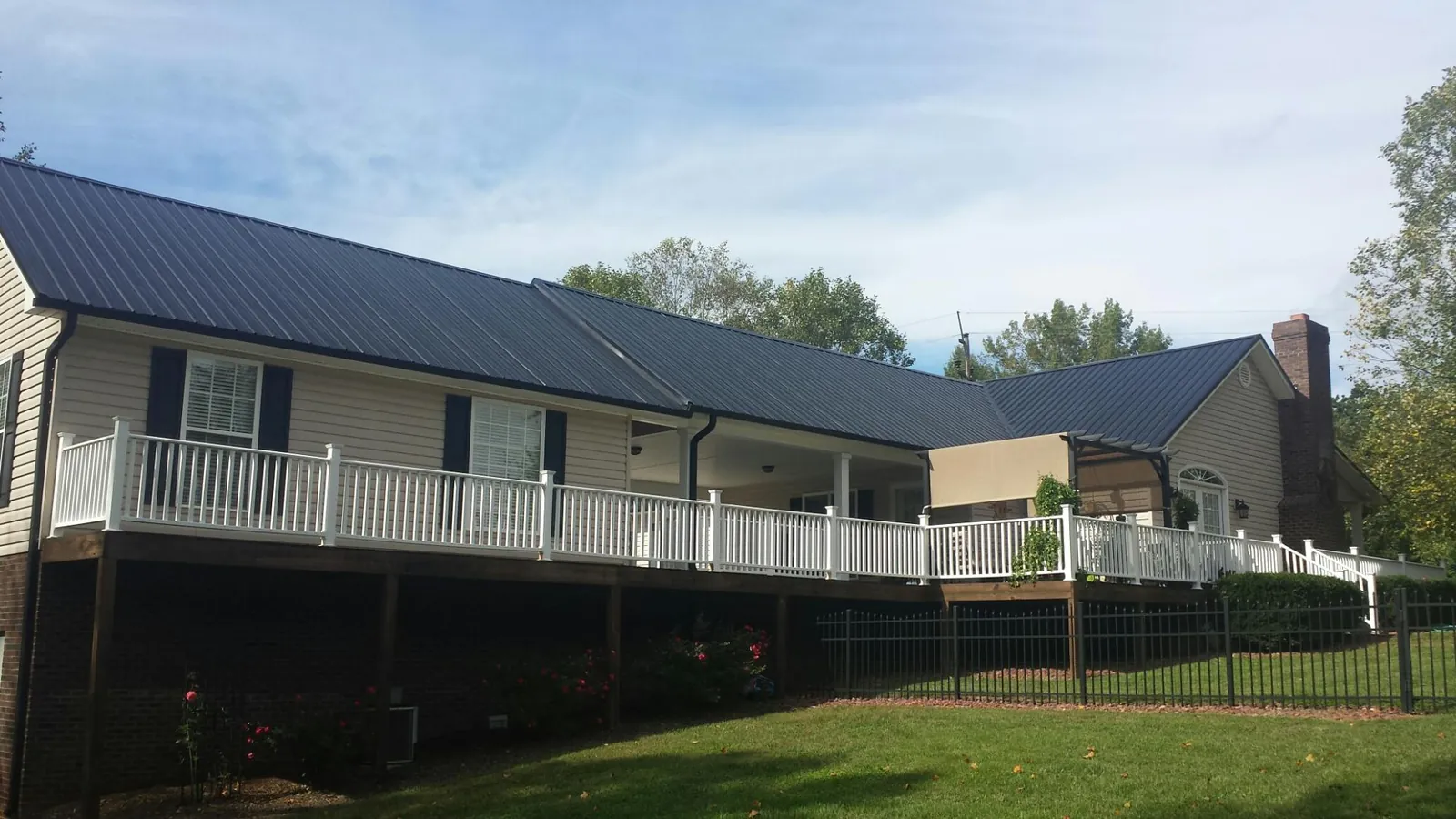 Black metal roof above a long white railed deck on a hillside home in Hiawassee