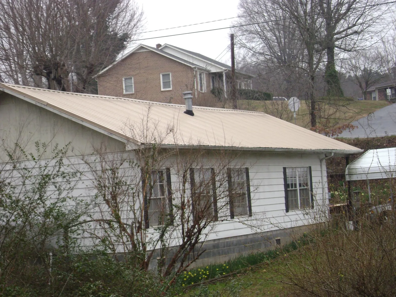 Tan metal roof on a white sided house set into a hillside — Commercial Roofing by Roofing Brothers in Hiawassee