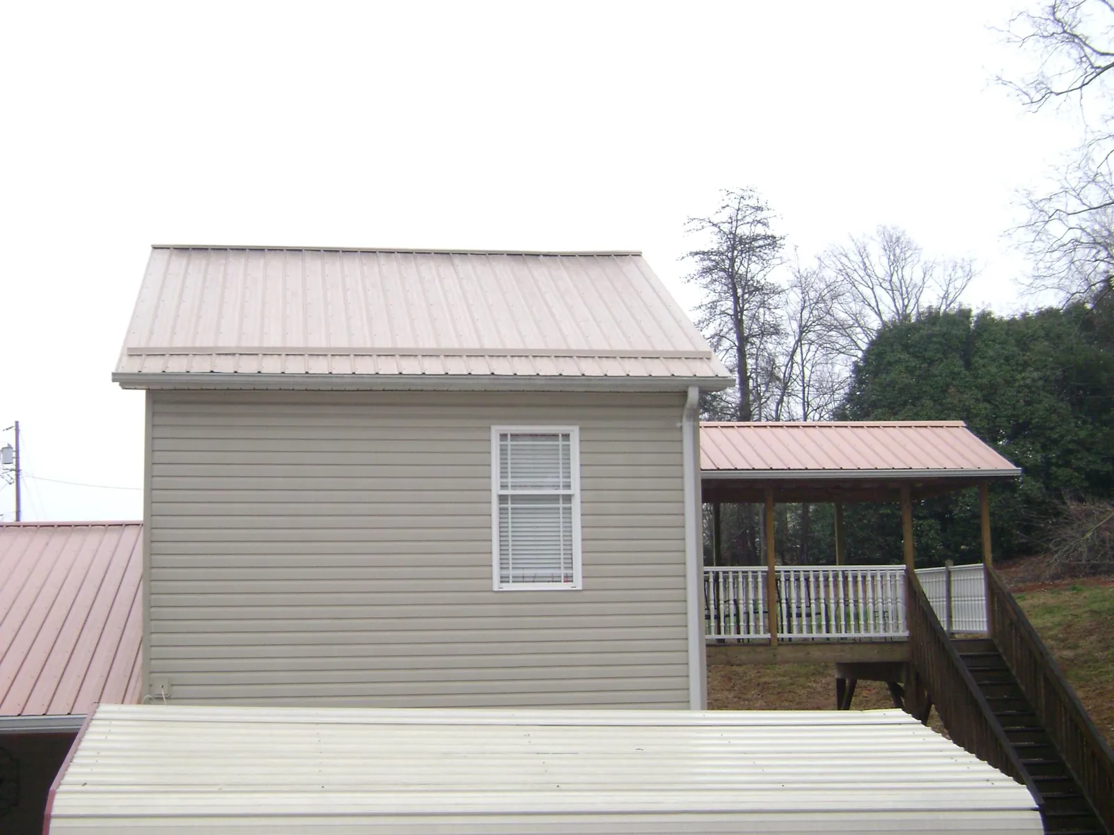 Tan metal roofs on a two story addition and attached porch, from a Roof Replacement job in Hiawassee